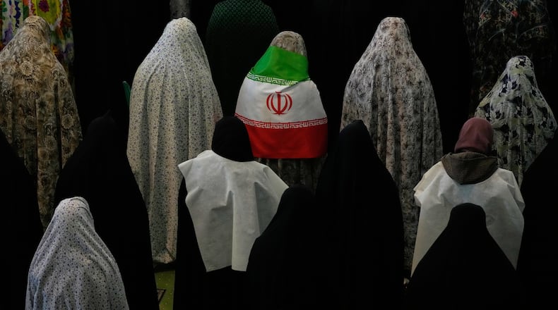 Iranian worshippers perform Eid al-Fitr prayers marking the end of the holy fasting month of Ramadan as one of them wears an Iranian flag at the Imam Khomeini Grand Mosque in Tehran, Iran, Saturday, March 21, 2026. (AP Photo/Vahid Salemi)