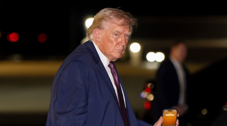 President Donald Trump holds a cell phone with a call to Nvidia CEO Jensen Huang as he departs on Air Force One at Rocky Mount-Wilson Regional Airport, Friday, Dec. 19, 2025, in Elm City, N.C. (AP Photo/Alex Brandon)