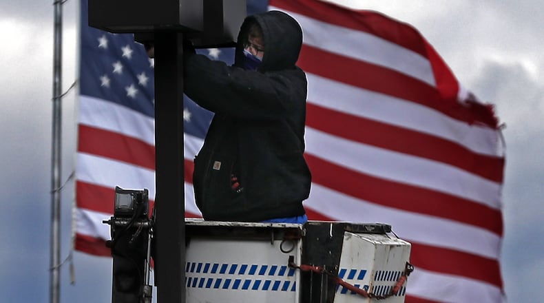 The giant American flag at the Springfield Post Office provided a patriotic backdrop for a worker fixing a light in the parking lot of Shawnee Place Apartments in downtown Springfield. BILL LACKEY/STAFF
