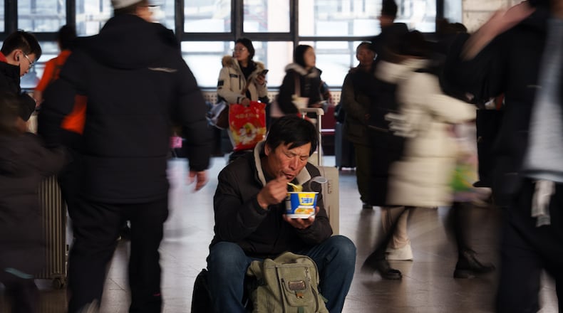 A traveler eats while waiting inside a railway station as people return home during the Lunar New Year holiday in Beijing, China, Tuesday, Feb. 10, 2026. (AP Photo/Vincent Thian)