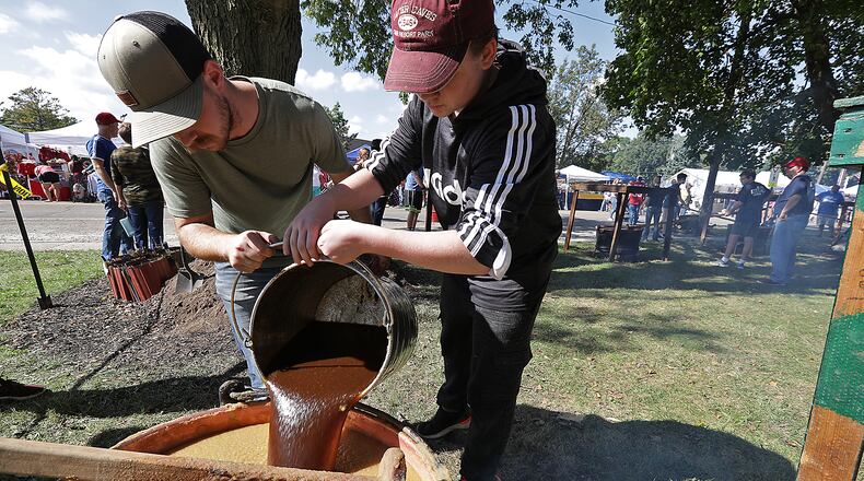 Jacob Juergens, left, and Caelek Stephany, both members of the Murphy family, pour the brown sugar mixture into one of the cauldrons of cooking apple butter Saturday at the Enon Apple Butter Festival. BILL LACKEY/STAFF