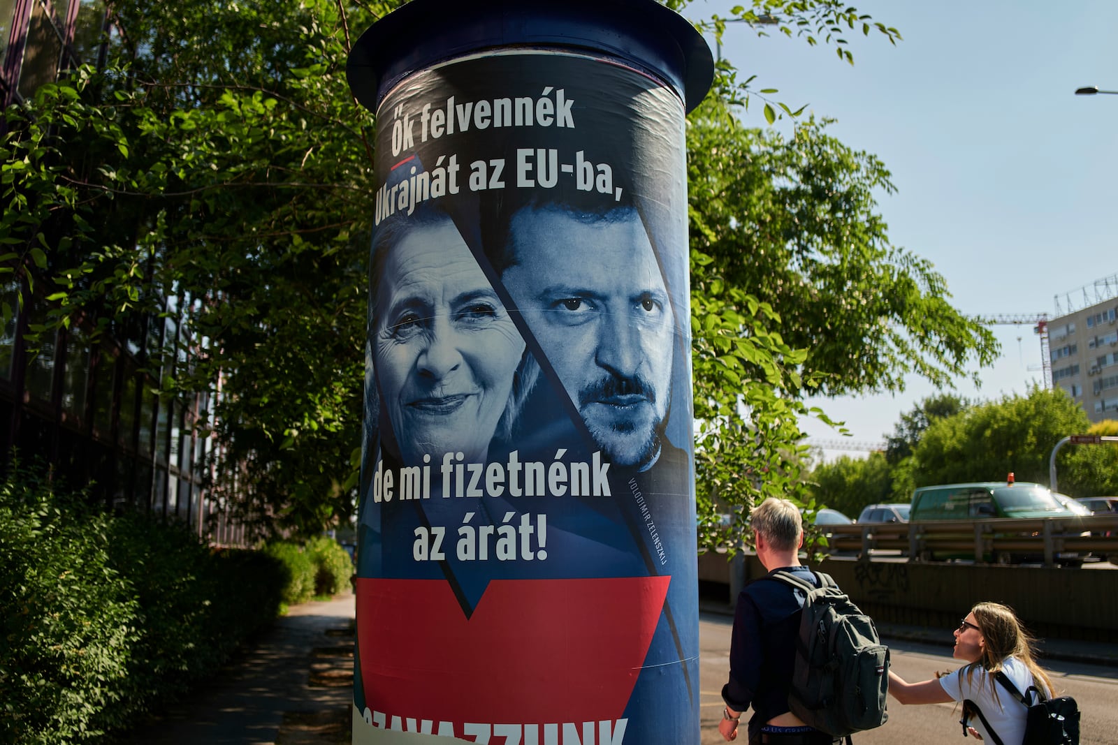 People pass by a Hungarian government billboard, opposing Ukraine's EU membership, showing European Commission President Ursula von der Leyen and Ukrainian President Volodymyr Zelenskyy, which reads "They would bring Ukraine into the EU, but we would pay the price! Let's vote no!", In Budapest, Hungary, Wednesday, June 11, 2025. (AP Photo/Bela Szandelszky)