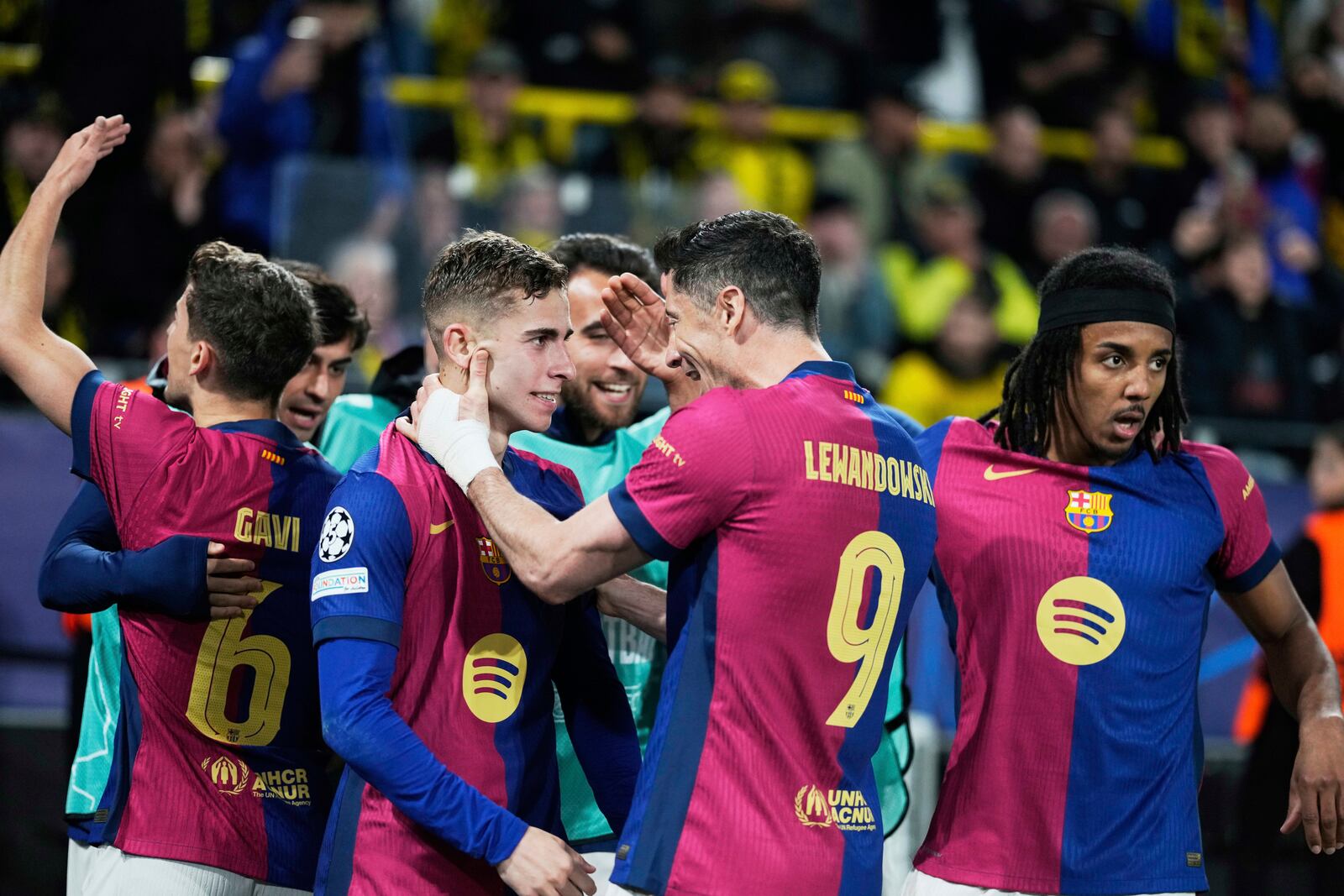 Barcelona's Robert Lewandowski (9) and Fermin Lopez celebrate after forcing an own goal by Dortmund's Ramy Bensebaini during the Champions League quarterfinals second leg soccer match between Borussia Dortmund and Barcelona, at the Signa-Iduna Park in Dortmund, Germany, Tuesday, April 15, 2025. (AP Photo/Matthias Schrader)