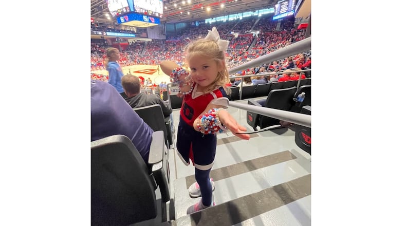 Dayton fan Caroline Kremer, 4, shows off the friendship bracelets she made for the Flyers players and cheerleaders at UD Arena during a game in 2025. Contributed photo