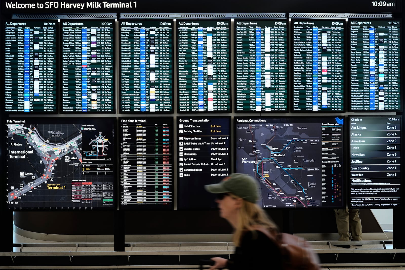 A traveler walks past screens showing outgoing and incoming flights at San Francisco International Airport ahead of the Memorial Day holiday weekend in San Francisco, Thursday, May 22, 2025. (AP Photo/Godofredo A. Vásquez)
