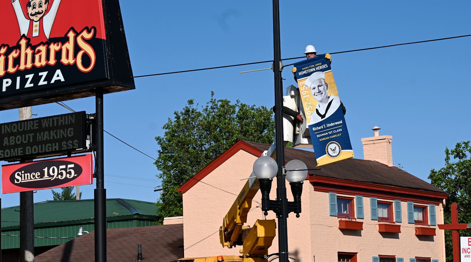 Pictured Travis Jenkins, an employee with the Hamilton Department of Infrastructure, installing on Wednesday, April 30, 2025, the Hometown Hero banner of the late Richard Underwood, the founder of Richard's Pizza. His banner is in front of the pizzeria he built in 1969 on Main Street. There will be more than 620 Hometown Hero banners installed around the city and on display until Veterans Day, Nov. 11, 2025. MICHAEL D. PITMAN/STAFF