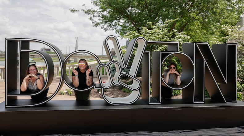 Left to right, SarahLydia Keihl (City of Dayton, Public Affairs), Jes Sands (Downtown Dayton Partnership), and Megan Peters (Cross Street Partners) take a photo at the newly unveiled Dayton Peace Sign on Thursday, May 15, 2025, at RiverScape MetroPark Festival Plaza. JOSEPH COOKE/STAFF