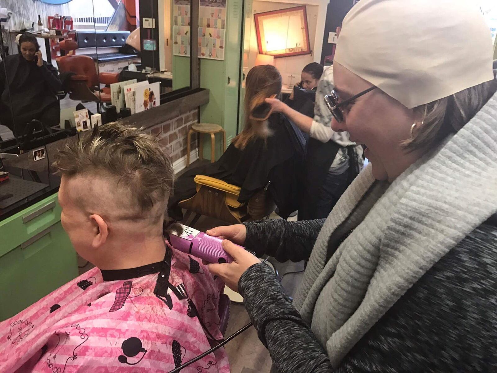 Alexis Larsen (right) takes a turn shaving Kristen Wicker’s head during a head-shaving shindig at Derailed Hair Salon in the Oregon District. CONTRIBUTED