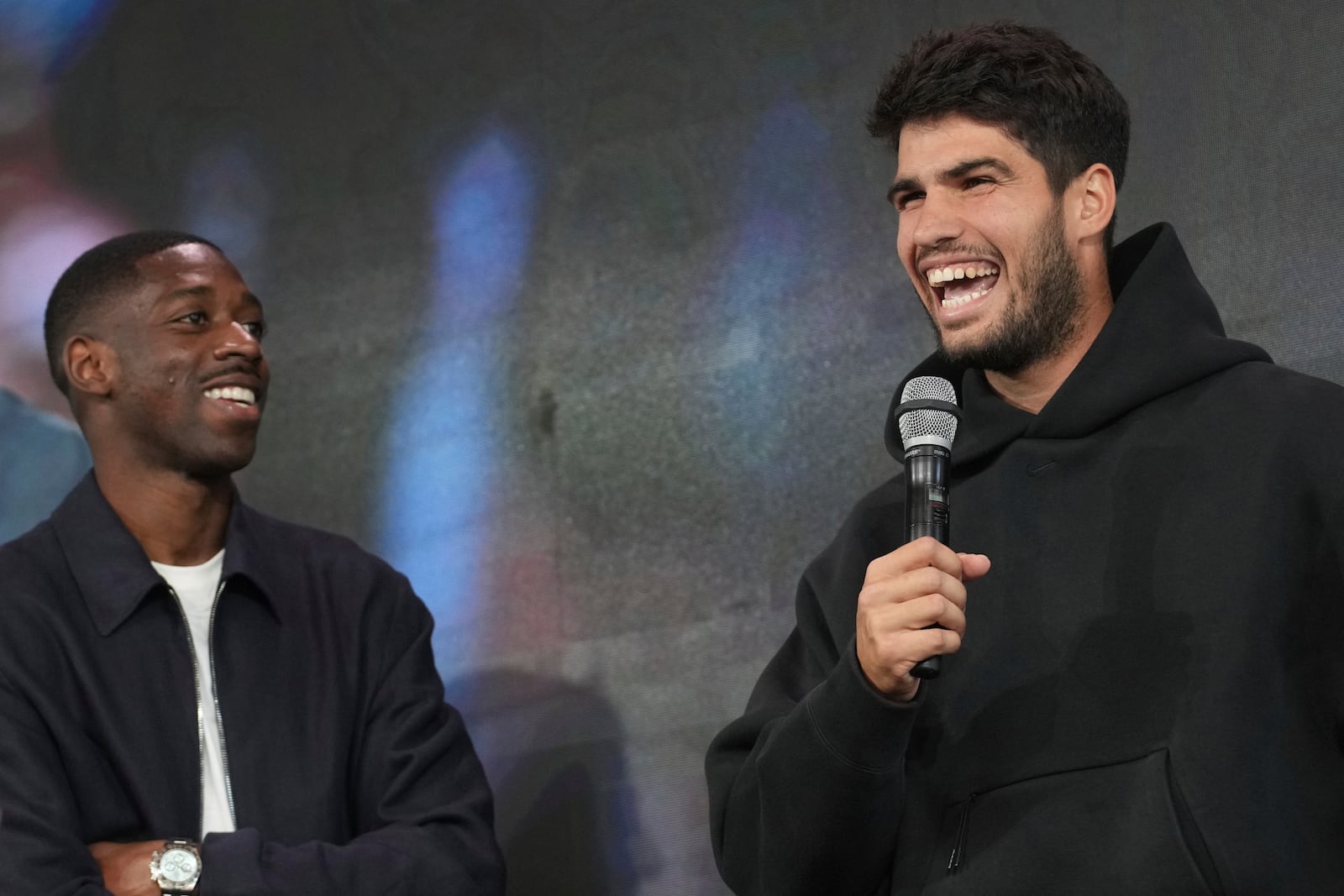 Titleholder Carlos Alcaraz, of Spain, speaks during the draw of French Open tennis tournament while PSG soccer player Ousmane Dembele looks on, Thursday, May 22, 2025 at the Roland Garros stadium in Paris. (AP Photo/Christophe Ena)