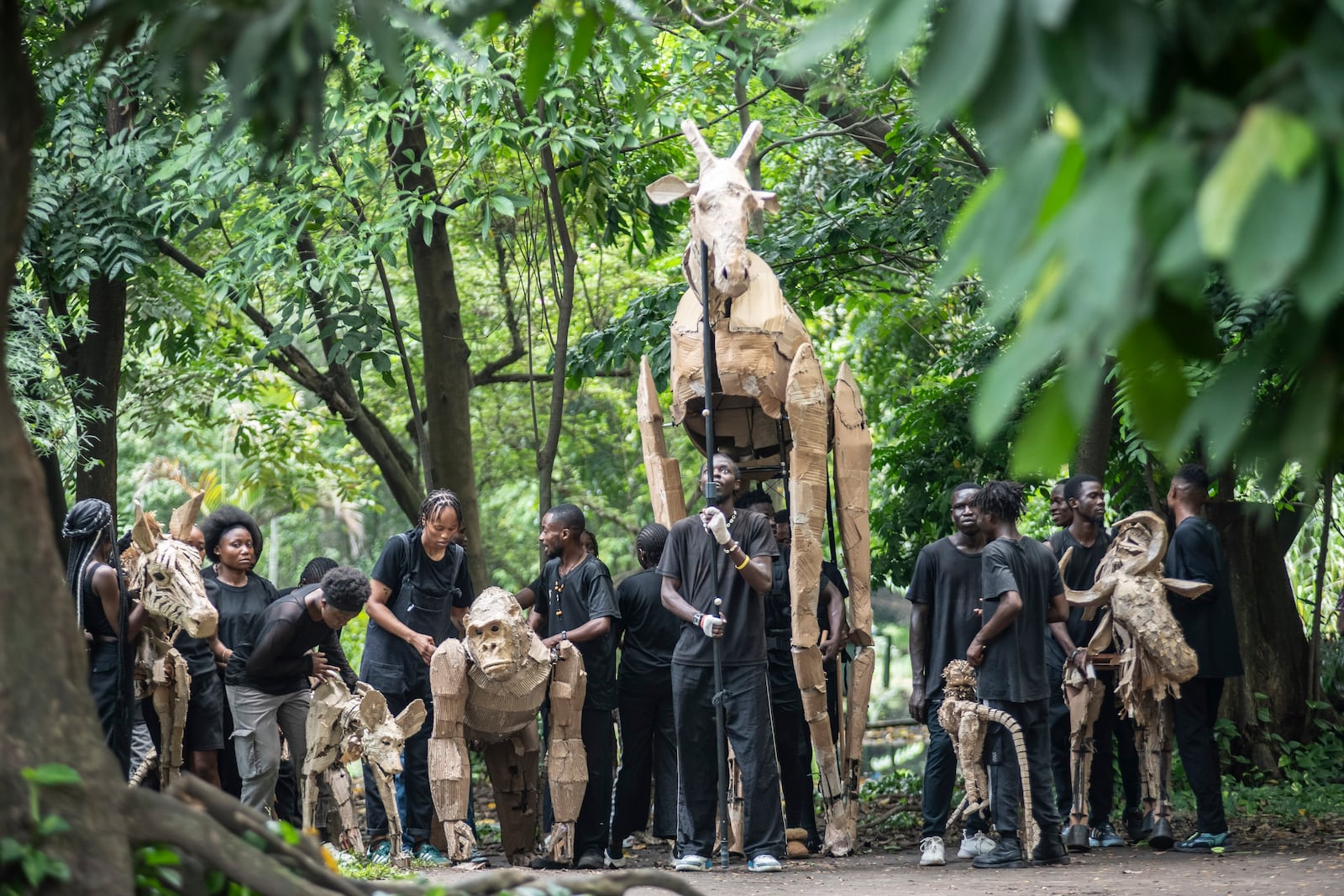 Puppeteers move cardboard animals through DRC's capital Kinshasa's botanical gardens Thursday, April 10, 2025, the first steps of "The Herds", a moving theatre performance that will travel from the Democratic Republic of the Congo to the Arctic Circle in a bid to bring attention to the climate crisis. (AP Photo/Samy Ntumba Shambuyi)