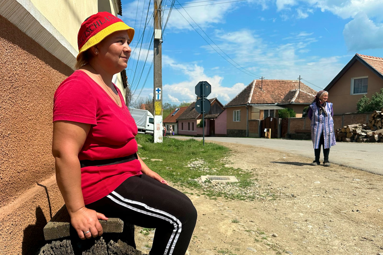 Monica Rosalea, 41, who periodically works abroad, sits on a wooden bench in the village of Saschiz, in Romania's central Transylvania region, Friday, April 25, 2025. (AP Photo/Stephen McGrath)