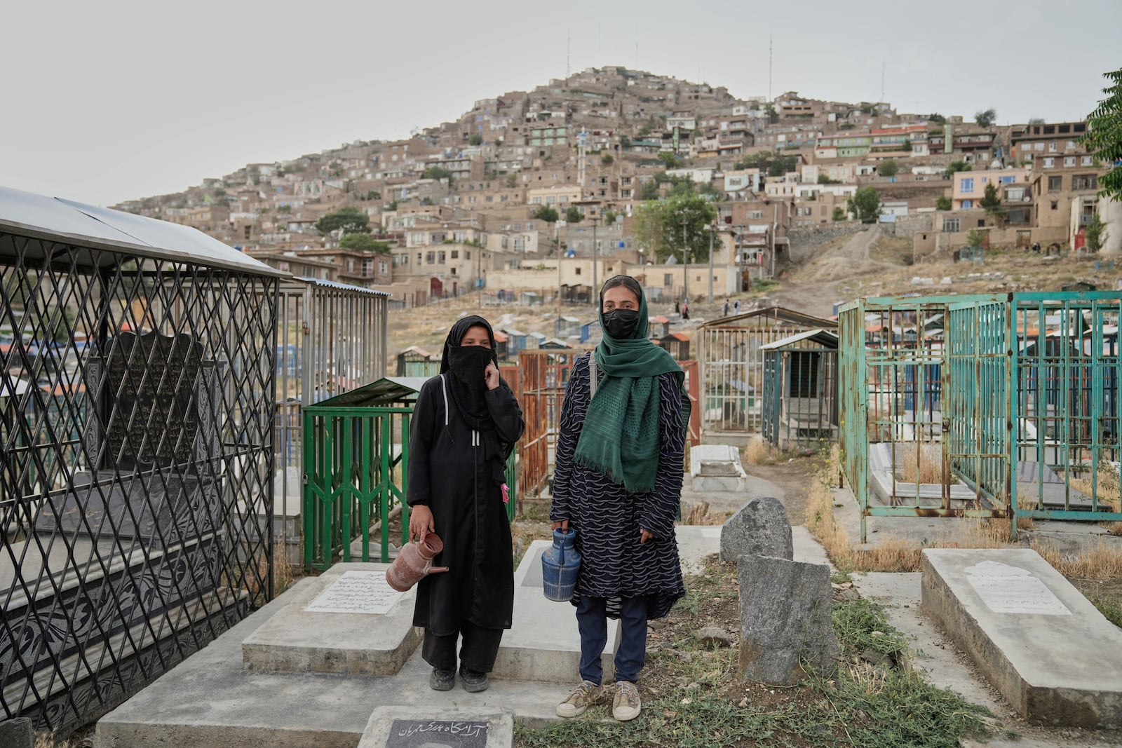 Nahideh, 13, left, an Afghan girl, stands with her friend as they wait for customers to buy water at a cemetery in Kabul, Afghanistan, Tuesday, May 27, 2025. (AP Photo/Ebrahim Noroozi)