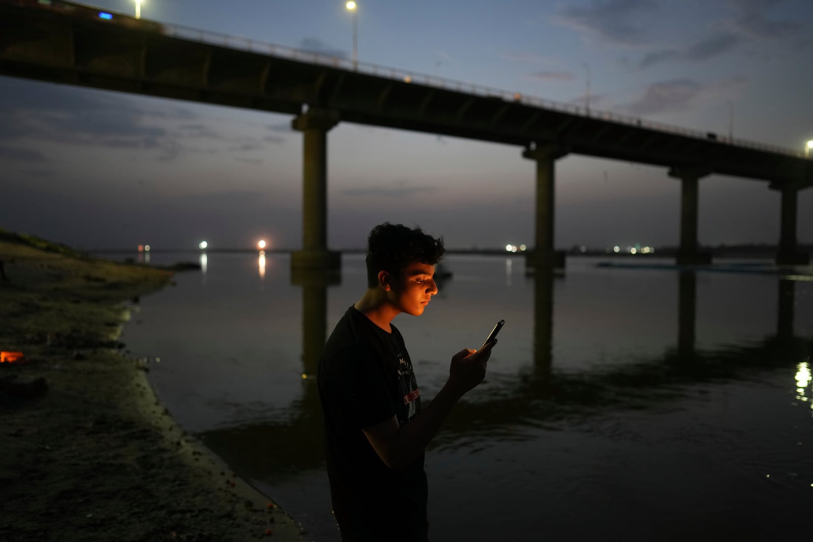 FILE - A youth checks his mobile phone on the bank of the River Ganges in Prayagraj, India, June 7, 2023. (AP Photo/Rajesh Kumar Singh, File)