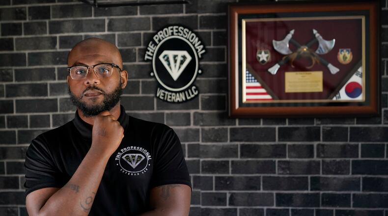 Phillip Slaughter, who served in the U.S. Army for 18 years, poses in his home Nov. 10, 2022, in Clarksville, Tenn. Framed on his wall on the right are memorabilia from a military assignment in South Korea where he worked as a logistics trainer. On the left is the logo for his company in which he helps service members transition into the civilian workforce. (AP Photo/Mark Humphrey)