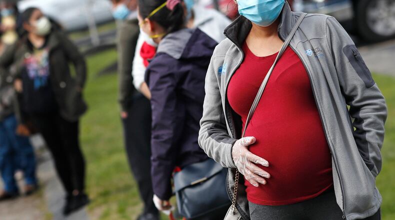 FILE - In this May 7, 2020 file photo, a pregnant woman wearing a face mask and gloves holds her belly as she waits in line for groceries at St. Mary's Church in Waltham, Mass. The Centers for Disease Control and Prevention urged all pregnant women Wednesday, Aug. 11, 2021 to get the COVID-19 vaccine as hospitals in hot spots around the U.S. see disturbingly high numbers of unvaccinated mothers-to-be seriously ill with the virus. (AP Photo/Charles Krupa, file)
