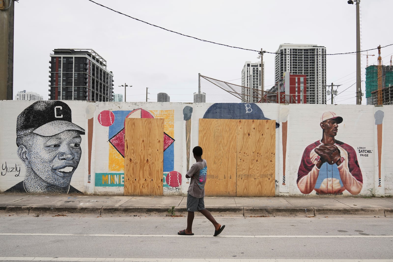 A person walks past murals of baseball legends Minnie Miñoso, second from left, and Jackie Robinson, second from right, covered with plywood after being defaced in Miami's Overtown neighborhood, Thursday, June 5, 2025, in Miami. (AP Photo/Lynne Sladky)