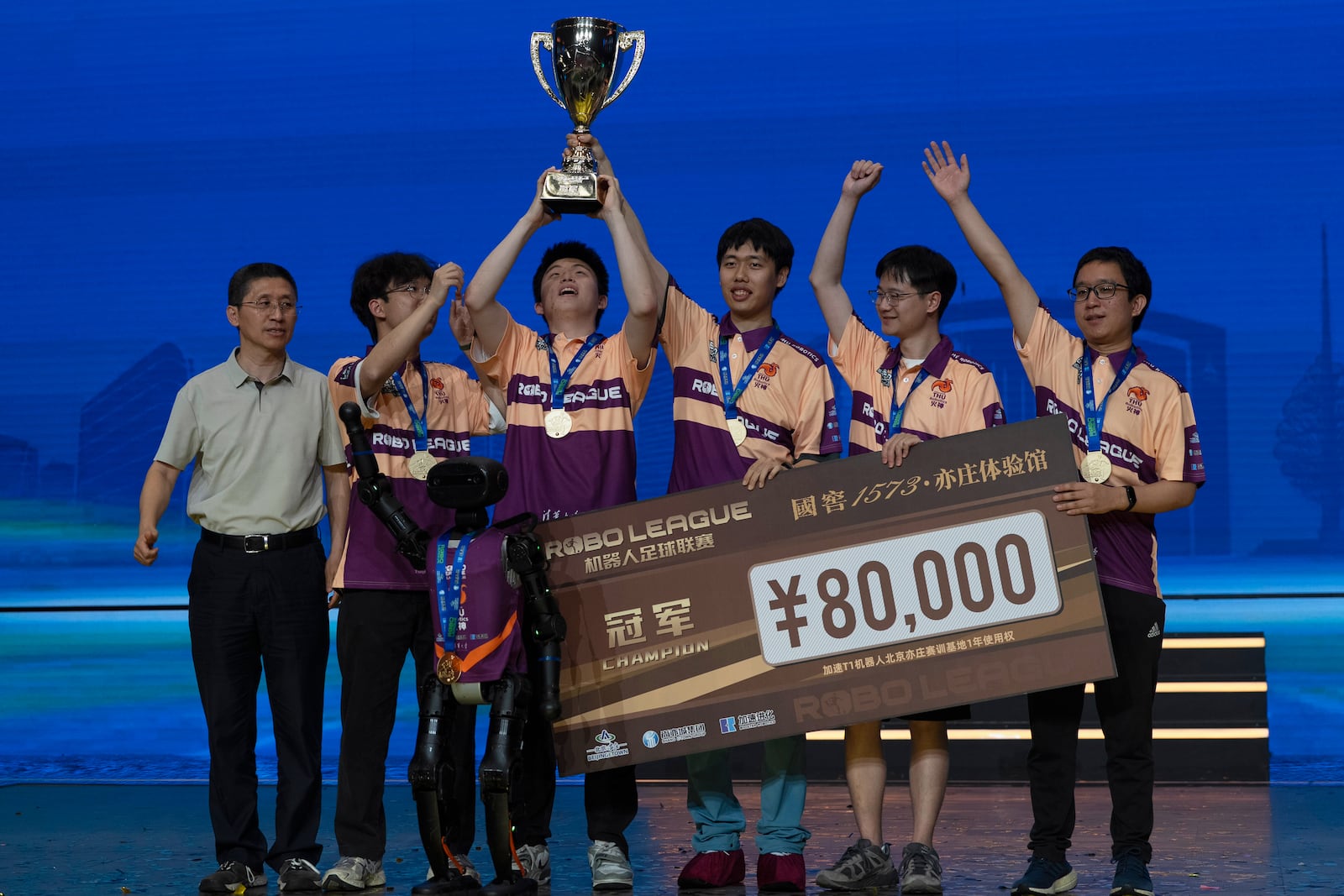 The human members of Team THU celebrate with their trophy near a T1 robot from Booster Robotics used during the inaugural RoBoLeague robot soccer competition held in Beijing, Saturday, June 28, 2025. (AP Photo/Ng Han Guan)