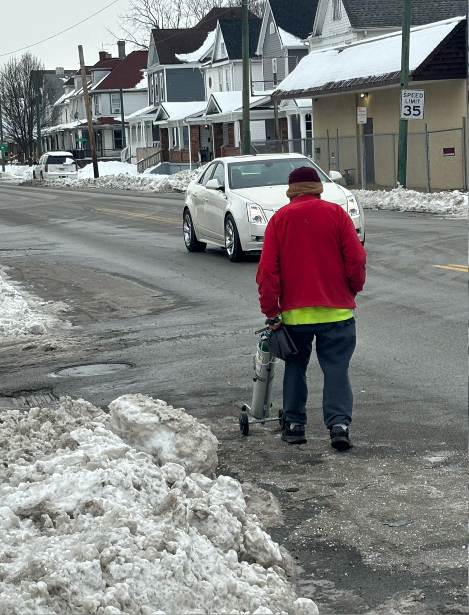 In a reader-submitted photo, a Dayton resident with an oxygen tank is forced to walk in the street due to snow-covered sidewalks at E. Third Street and S. Garland Avenue on Jan. 10, 2025. SAM HUIST, CONTRIBUTED