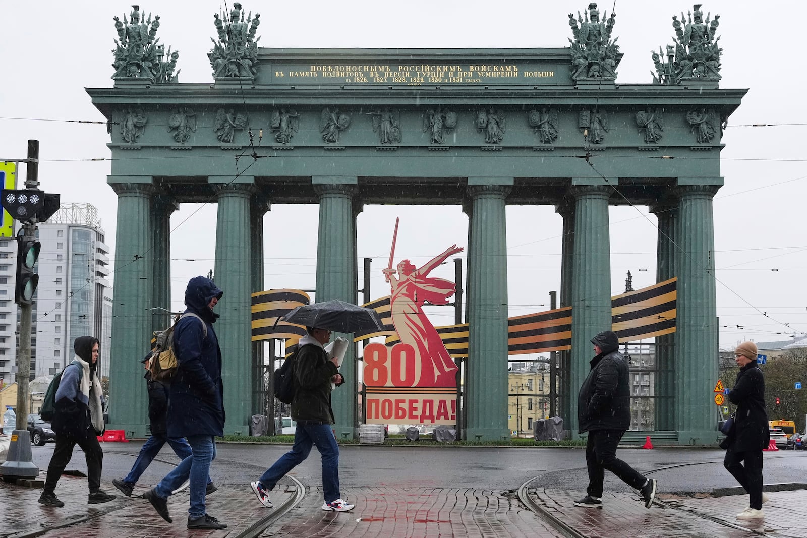 People cross the street past 'Moscow's Triumphal Gate' decorated with a large-scale composition depicting a replica of the 'Motherland Calls' monument ahead of celebrations of the 80th anniversary of the Soviet Union's victory over Nazi Germany during World War II in St. Petersburg, Russia, Monday, April 28, 2025. (AP Photo/Dmitri Lovetsky)