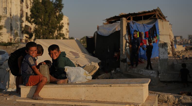 Palestinian children sit on a grave near makeshift tents for displaced people that were set up in a cemetery in Khan Younis, in the southern Gaza Strip, Friday, Oct. 31, 2025. (AP Photo/Abdel Kareem Hana)