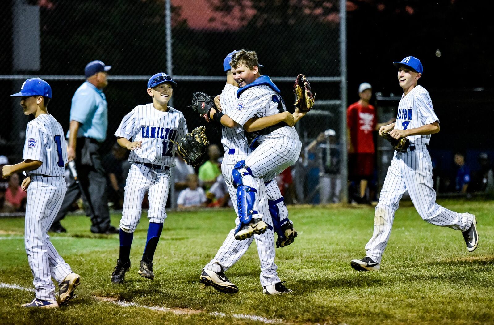 Hamilton West Side catcher Peyton Eldridge jumps up into the arms of pitcher Ethan Stone as they celebrate a 15-0 victory over Hamilton-Fairfield in Thursday night’s Little League District 9 championship game at West Side. NICK GRAHAM/STAFF