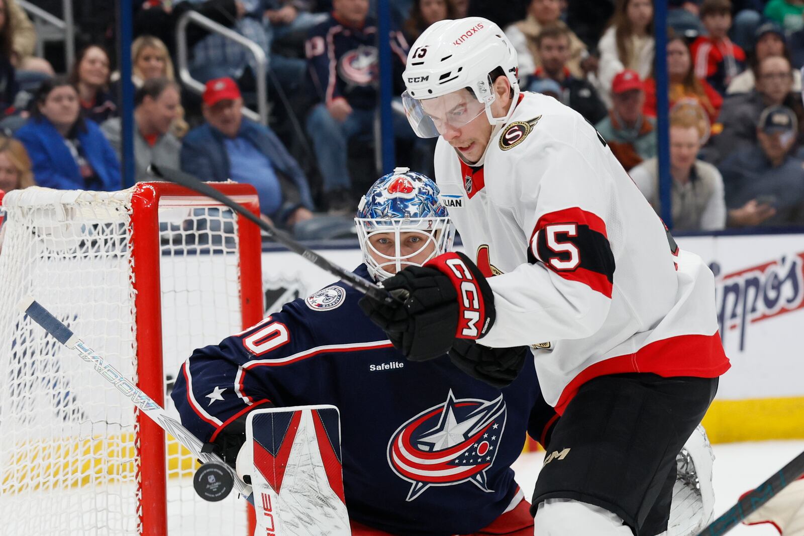 Columbus Blue Jackets' Elvis Merzlikins, left, knocks the puck away from Ottawa Senators' Matthew Highmore during the first period of an NHL hockey game Tuesday, April 8, 2025, in Columbus, Ohio. (AP Photo/Jay LaPrete)