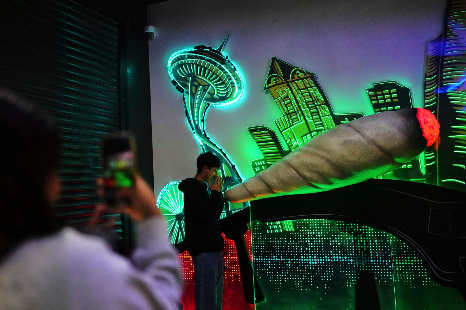 Gabriel Ramos poses for a photo in front of a large marijuana cigarette and downtown Seattle mural as Sarah Vargas takes a photo at Have a Heart cannabis dispensary Sunday, April 20, 2025, in Seattle. (AP Photo/Lindsey Wasson)