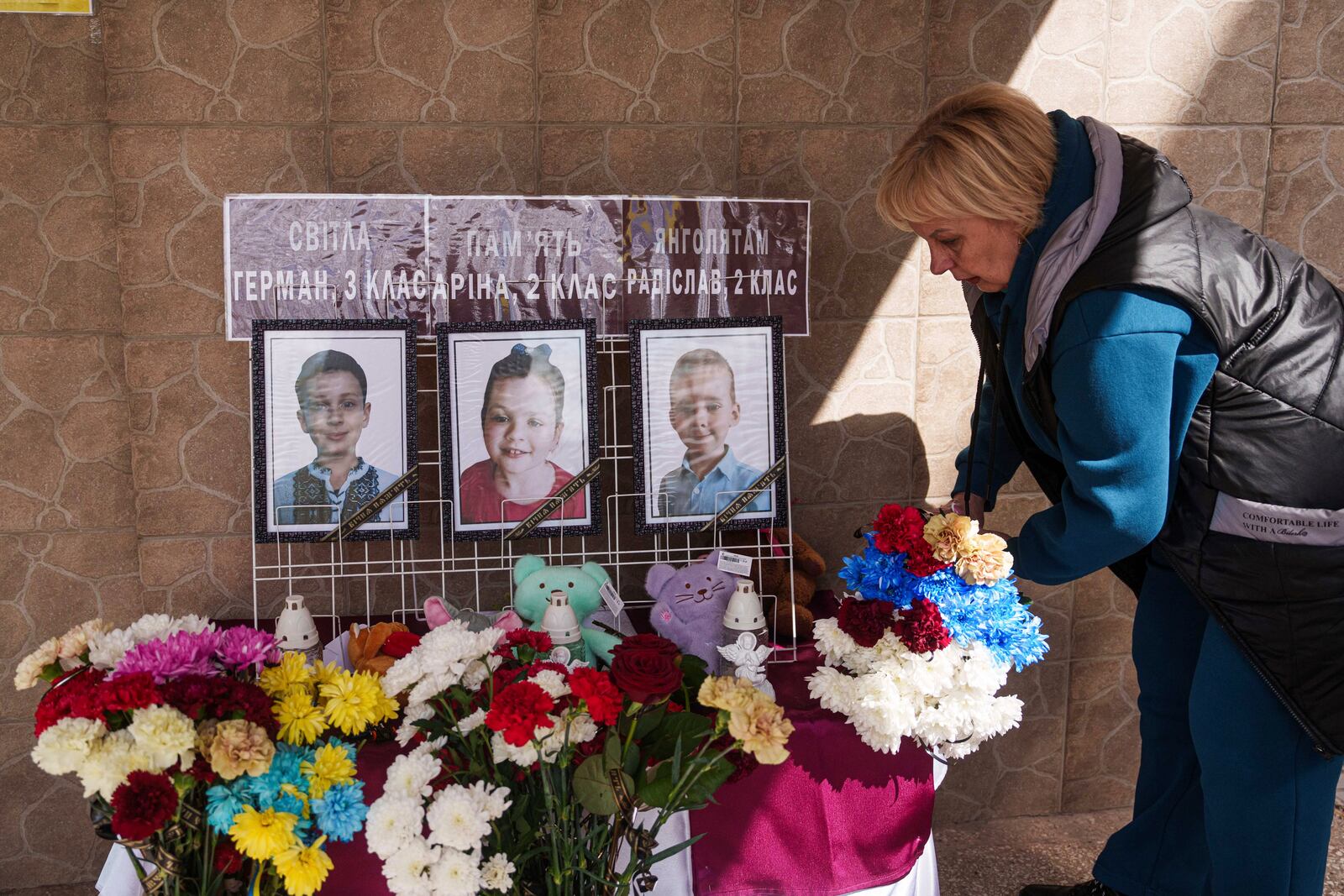 A woman puts flowers on a memorial wall during the farewell ceremony for three schoolchildren from 41st school killed by a Russian Rocket strike in Kryvyi Rih, Ukraine, Monday, April 7, 2025. (AP Photo/Evgeniy Maloletka)