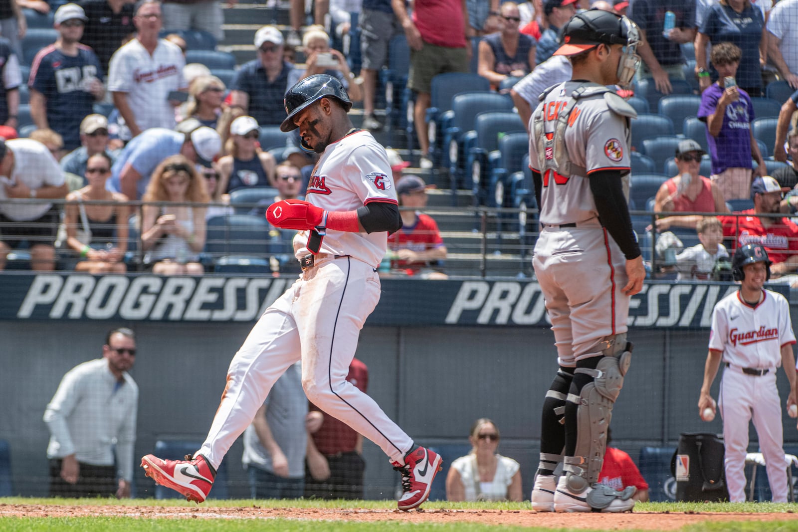 Cleveland Guardians' Angel Martinez, left, scores on a sacrifice fly by Nolan Jones as Baltimore Orioles' Alex Jackson looks towards the field during the third inning of a baseball game, Thursday, July 24, 2025, in Cleveland. (AP Photo/Phil Long)