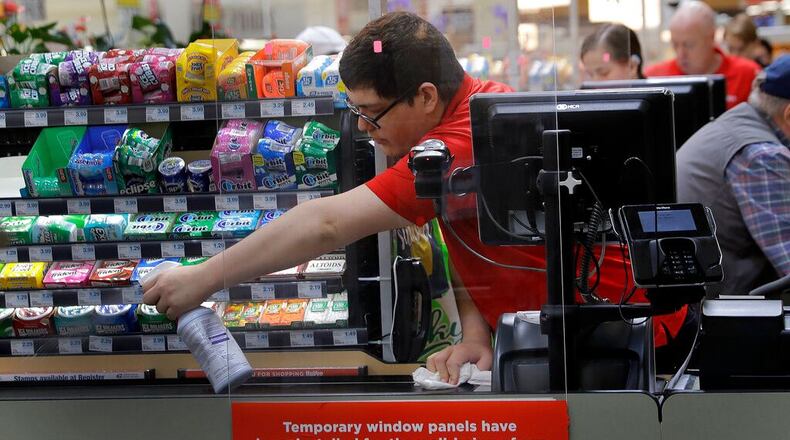 Garrett Ward sprays disinfectant on a conveyor belt between checking out shoppers behind a plexiglass panel at a Hy-Vee grocery store Thursday, March 26, 2020 in Overland Park, Kan. Stores have begun installing the shields in checkout aisles as a precaution to protect clerks and help stop the spread the new coronavirus.