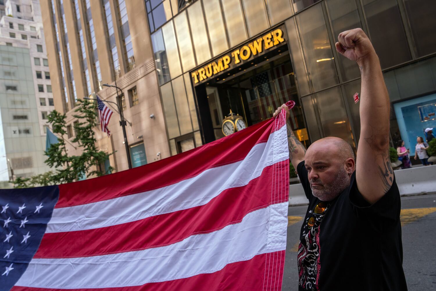 
                        A supporter of former President Donald Trump helps to unfurl an oversized United States flag outside Trump Tower in midtown Manhattan on Sunday morning, July 14, 2024, one day after Trump was shot while speaking at a campaign rally in Butler, Pa. Trump was declared “fine” by his campaign, and the gunman was killed by Secret Service snipers. The explosion of political violence further inflamed the campaign for the White House.  (Adam Gray/The New York Times)
                      