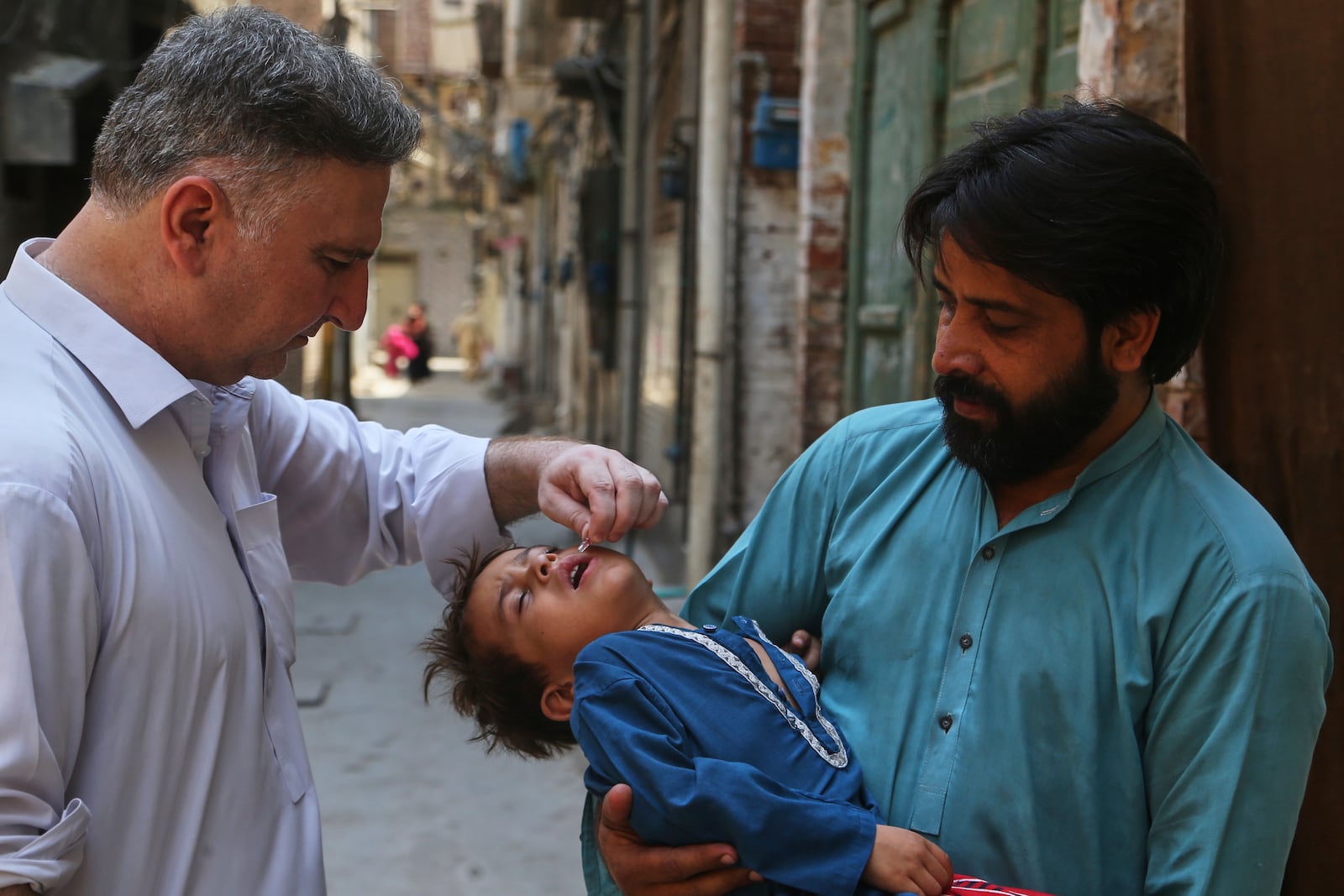 A health worker, left, administers a polio vaccine to a child at a neighborhood in Peshawar, Pakistan, Monday, May 26, 2025. (AP Photo/Muhammad Sajjad)