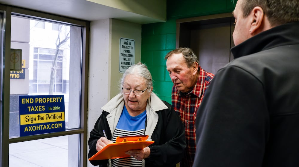 Jim Fescina, right, with AxOhioTax, gets signatures from Rob and Belinda Batdorf as they go in to pay taxes Thursday, Feb. 26, 2026 at Butler County Government Services Center building on High Street in Hamilton. AxOhioTax was collecting signatures in order to put property tax repeal on the November ballot. NICK GRAHAM/STAFF