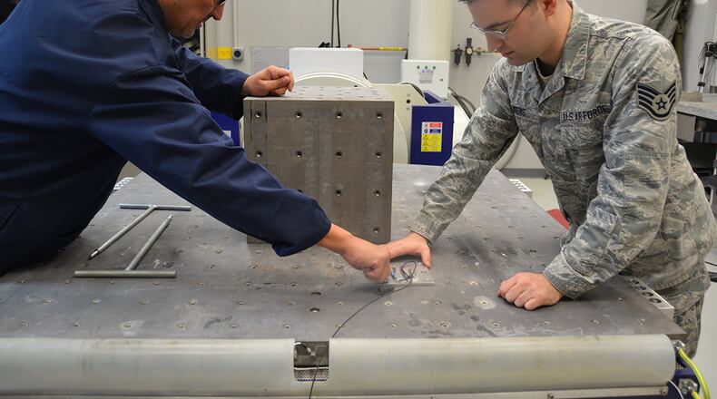 David Ryerse, Air Force Life Cycle Management Center biomedical technician, and Staff Sgt. Taylor Wiens, 711th Human Performance Wing research scientist, mount a sensor designed to measure acceleration on the Aeromedical Laboratory’s multi-axis table (“shake table”). (U.S. Air Force photo/Gina M. Giardina)
