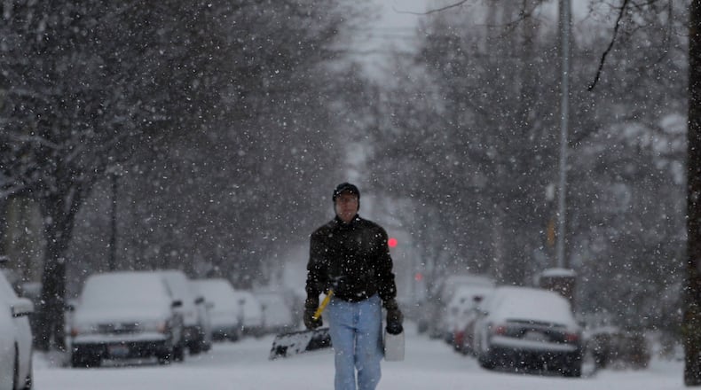 Jim Minutilli of Dayton carries a shovel and salt to take care of sidewalks covered with falling snow. STAFF PHOTO BY LISA POWELL