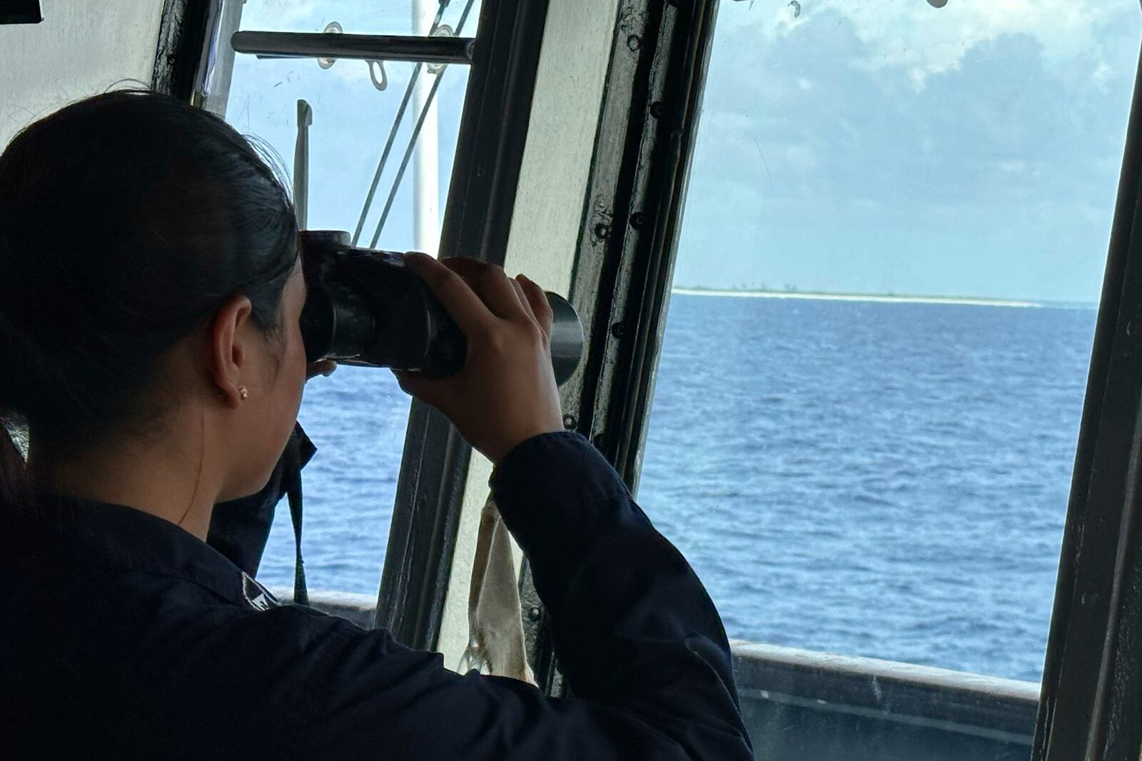 A member of the Philippine Navy uses binoculars as she looks at Northeast Cay, locally known as Parola Island, during a maritime patrol at the disputed South China Sea on Wednesday June 4, 2025. (AP Photo/Joeal Calupitan)