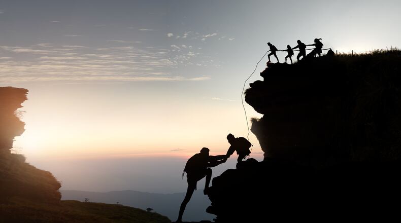 Hikers climbing up silhouette mountain cliff .