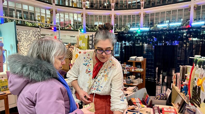 Kathleen Hotmer, owner of Pink Moon Goods in Dayton, helps a customer at her booth during HollyDays at the Dayton Arcade, Dec. 13, 2024. ALLISON SWANSON/STAFF
