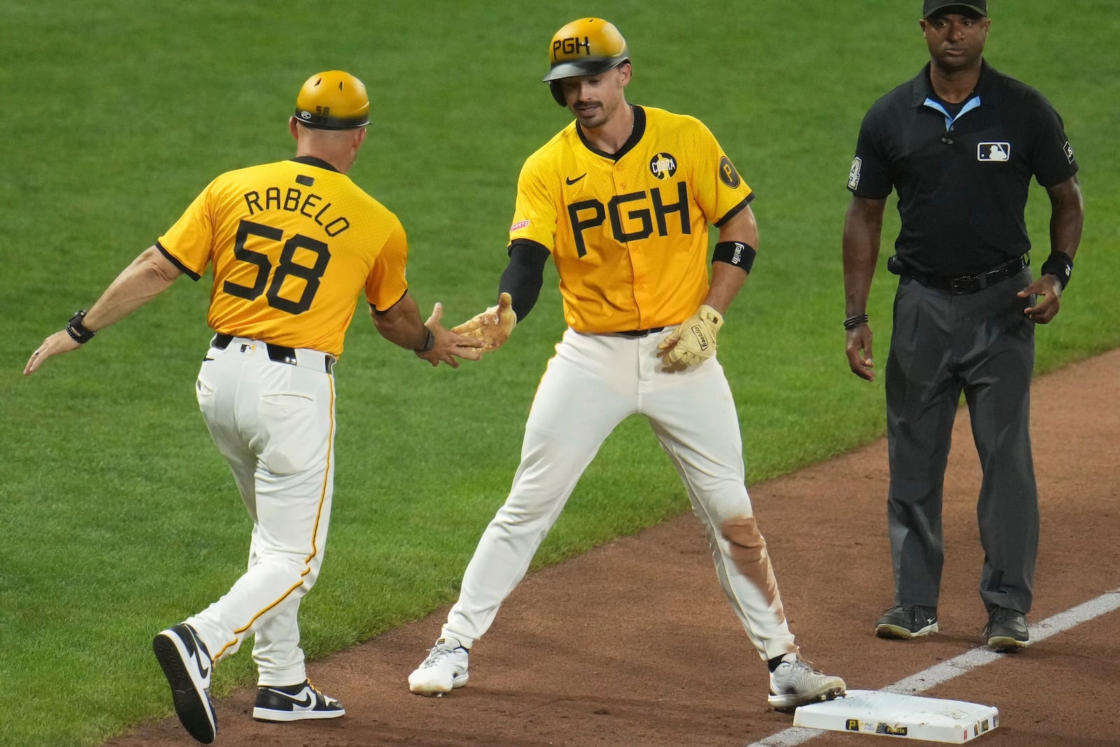 Pittsburgh Pirates' Bryan Reynolds, center, celebrates with third base coach Mike Rabelo (58) as Reynolds stands on third base after driving in two runs with a triple off Cincinnati Reds pitcher Tony Santillan during the eighth inning of a baseball game in Pittsburgh, Friday, Aug. 8, 2025. (AP Photo/Gene J. Puskar)
