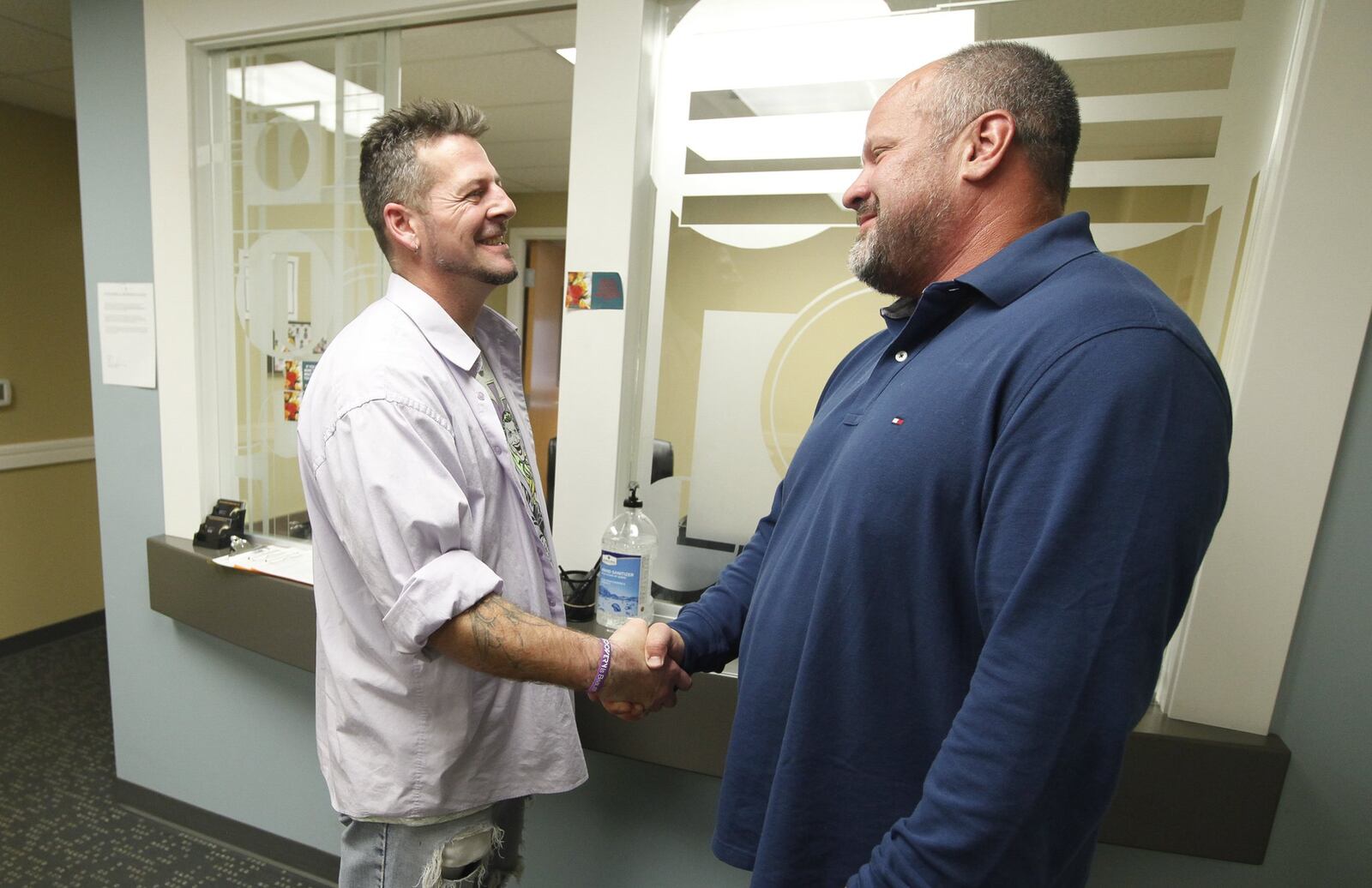 On his first anniversary clean of opioids, Scotty Mays, left, of Springboro is congratulated by Richard Confer, chief financial officer at Recovery Works Healing Center where Mays receives treatment. Mays’ past addiction was fueled by pain pills ordered on the “darknet” from China and delivered by the United States Postal Service to vacant houses where Mays or an acquaintance would gather the packages. CHRIS STEWART / STAFF