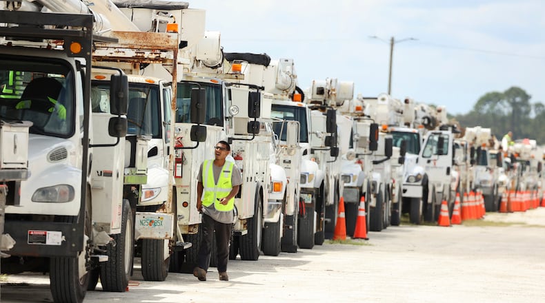 An electrical line technician walks among hundreds of electrical line trucks at Duke Energy's staging location in Sumterville, Fla., on Tuesday, Aug. 29, 2023. (Stephen M. Dowell /Orlando Sentinel via AP)