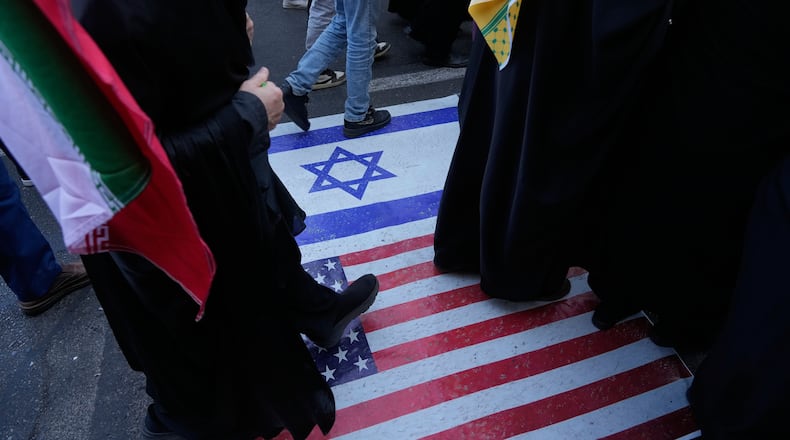 Demonstrators walk on a representation of the U.S. and Israeli flags during an annual rally in front of the former U.S. Embassy in Tehran, celebrating the anniversary of the 1979 takeover of the embassy, Iran, Tuesday, Nov. 4, 2025. (AP Photo/Vahid Salemi)