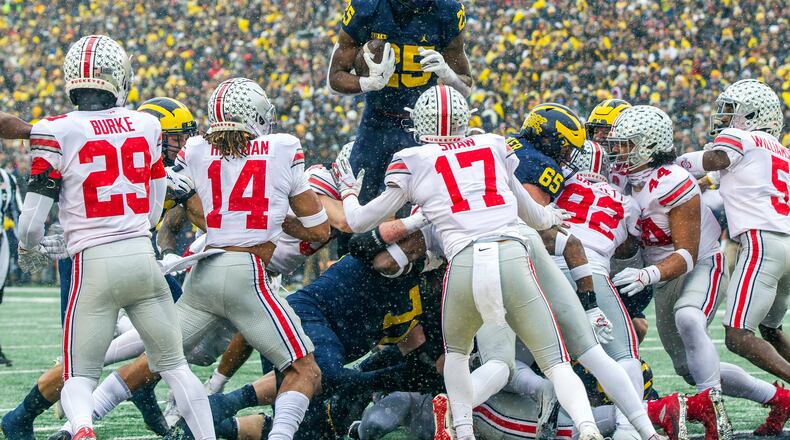 Michigan running back Hassan Haskins (25) leaps over Ohio State defenders for a touchdown in the second quarter of an NCAA college football game in Ann Arbor, Mich., Saturday, Nov. 27, 2021. (AP Photo/Tony Ding)