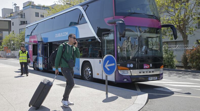 A man waits with his luggage at a Ouibus station in Paris, France, Tuesday, May 9, 2017. They're dubbed the Macron buses, cheap long-distance rides across France that were among Emmanuel Macron's few notable achievements before his meteoric rise to the French presidency, part of his efforts to loosen up the monopolized transport sector and invigorate the French economy. (AP Photo/Michel Euler)