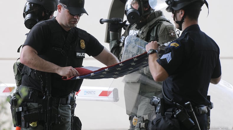 Members of the Dayton Police Department fold the American flag that they recovered from protesters Saturday. Protesters cut the rope to the flag, then took it down the Safety Building. MARSHALL GORBY\STAFF