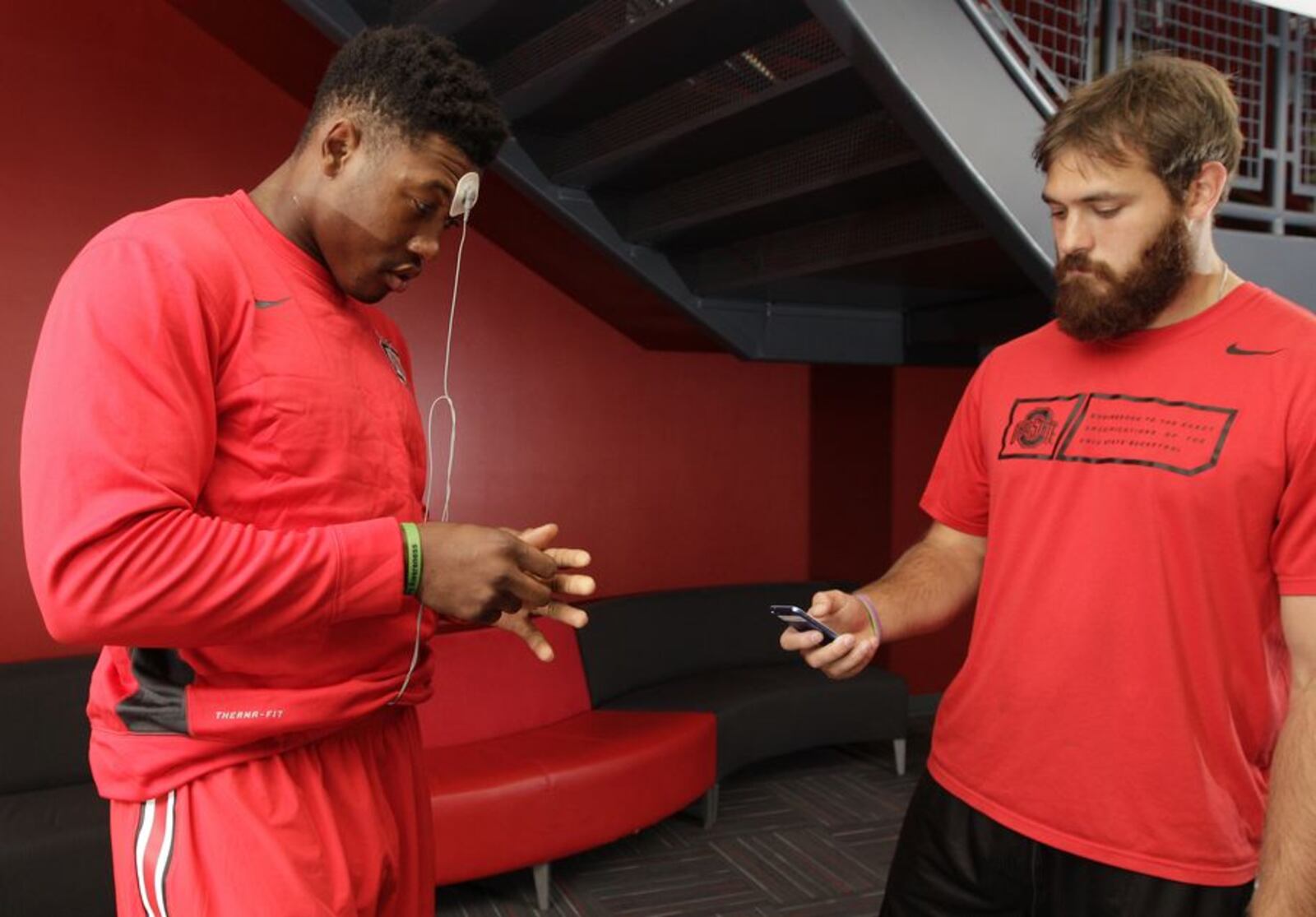 In this Sept. 16, 2015, photo, Ohio State strength and conditioning intern Mark Kulbis, right, helps linebacker Joshua Perry attach electrodes to his forehead and hand to start Perry's daily biometrics monitoring before practice in Columbus, Ohio. Ohio State uses the device to track overall physiological readiness of players and how they hold up to the wear and tear of football. (AP Photo/Jay LaPrete)