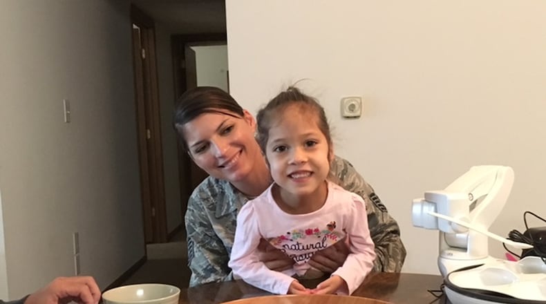 Grace Golembiewski, 3, sitting on the lap of her mother, Air Force Tech Sgt. Amada Golembiewski, often uses the “Obi” robot, seen to their left. With a programmable robotic arm, the Obi helps Grace (who has mobility challenges) eat with her family, her parents said. THOMAS GNAU/STAFF