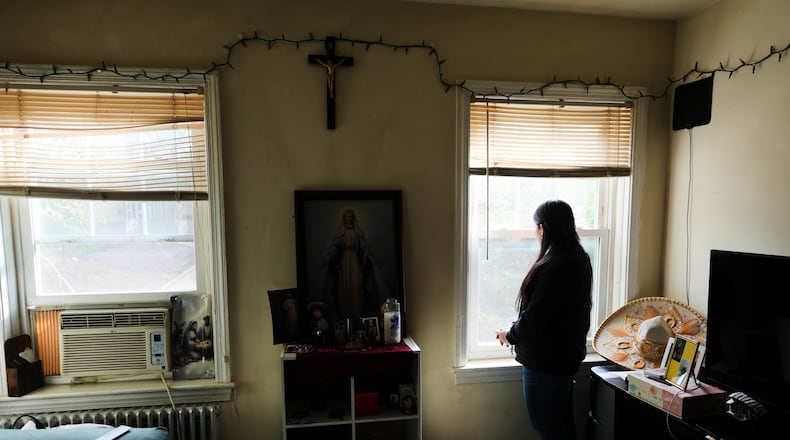A parishioner of the Shrine of the Sacred Heart, whose husband was detained by immigration agents, looks out her home's window as she poses for a portrait in Washington, Friday, Oct. 10, 2025. (AP Photo/Luis Andres Henao)