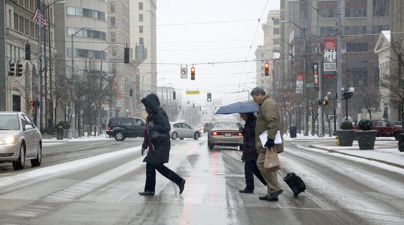 Pedestrians make their way through downtown Dayton as snow falls across the Miami Valley. LISA POWELL / STAFF FILE