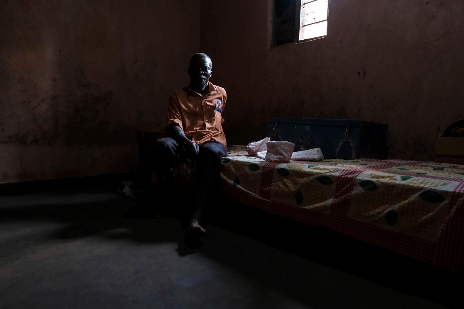 Simon Tigawalana sits on a bed as he rests his feet on a clay-based earthen floor made by EarthEnable at home on May 16, 2025, in Jinja, Uganda. (AP Photo/Hajarah Nalwadda)